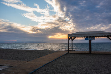 A wooden path leads to a gazebo by the sea.