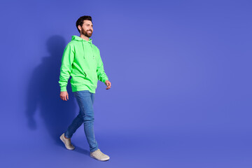 Full body photo of attractive young man walking empty space dressed stylish green clothes isolated on violet color background
