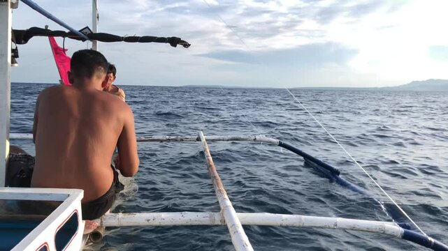 Fishermen are deploying a mile-long nylon fishing net in the sea from a wooden boat.