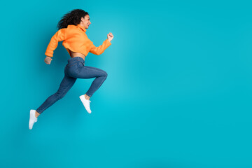 Full length photo of charming positive girl wear orange sweater jumping high running empty space...