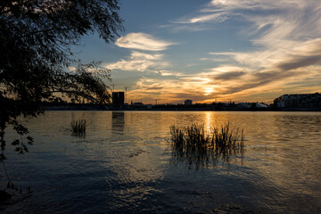 Golden sunset over calm river, framed by trees and reeds
