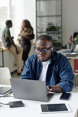 Vertical shot of African American man sitting at work desk and typing on keyboard while listening to music