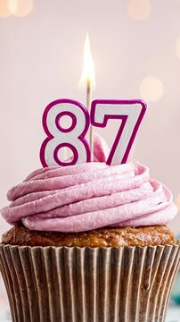 Birthday cupcake with burning lit candle with number 87. Number eighty-seven for eighty-seven years or eighty-seventh anniversary.
