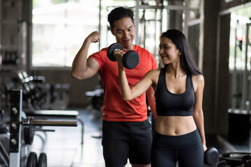 Fototapeta premium Young Asian woman raise dumbbell with boyfriend in gym