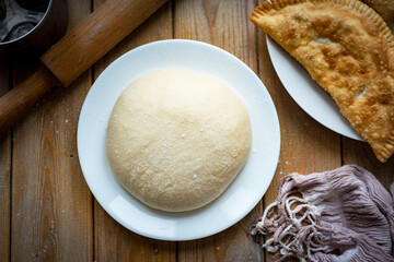 The dough for making chebureks on a white plate on a wooden table. Close-up.
