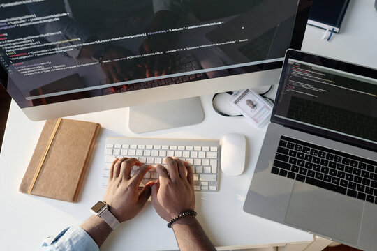 Top down shot of unrecognizable male hands typing on silver white keyboard on table top