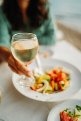 Young caucasian woman eating greek salad and drinking wine by the sea