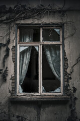 Mystery horror window exterior with broken glass. Abandoned house. Old and worn window frame exterior with broken glass and cracked wall. Dirty old white curtain. Dry vines