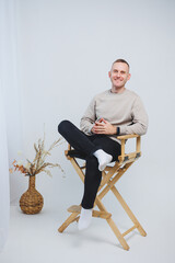 A young man sits on a chair and shows his emotions to the camera.