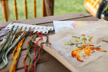 Close-up of a cross-stitch in progress. Cross-stitch with various colorful threads, a needle, and a pair of embroidery scissors. Intricate embroidery details, as well as the sewing process.