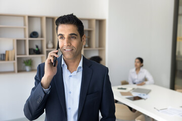 Young Indian male consultant distracted from group work in office make answer customers phone call....
