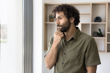 Pensive young businessman of Arabic ethnicity lost in thoughts try to predict future sales result. Thoughtful male financial analyst hesitate pondering on new possibilities of risky business solution