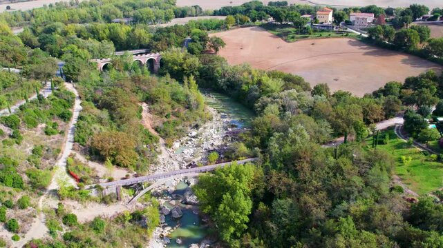 Bagno Vignoni&rsquo;s natural beauty captured with a winding path through rocky terrain and greenery, offering a peaceful escape into nature under a bright blue sky