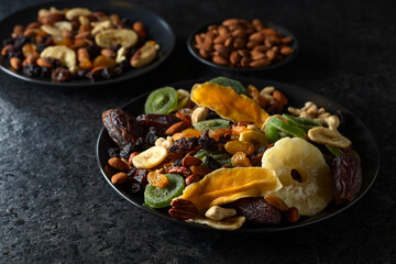 Dried tropical fruits, nuts, and raisins in black plate.