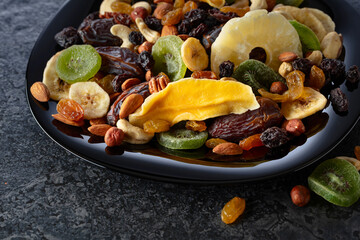 Dried tropical fruits, nuts, and raisins in black plate.