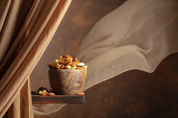 The mix of various nuts and raisins in a wooden bowl on a brown background.
