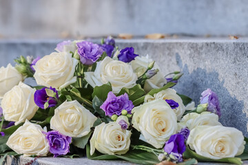 Flower arrangement of white roses and blue eustoma. A beautiful blue and white memorial bouquet has been placed on the stone steps at the memorial site in the cemetery.
