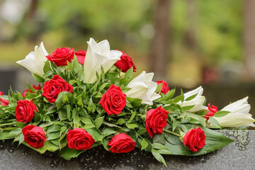 Flower arrangement. Red and white funeral flowers on a gravestone in a cemetery. Relatives have brought memorial flowers to the grave. Beautiful remembrance bouquet.