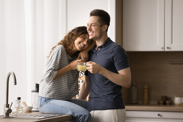 Happy married couple in love hugging in kitchen, drinking hot beverages, enjoying domestic leisure...