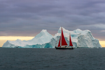 Red sailboat next to large iceberg in Disko Bay Greenland