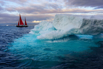 Red sailboat next to large iceberg in Disko Bay Greenland