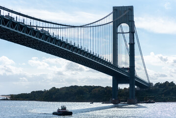 The Verrazzano-Narrows Bridge stretches across the Upper Bay near New York City, its steel arches silhouetted against a cloudy sky. The towering structure stands as a monumental gateway to the city.