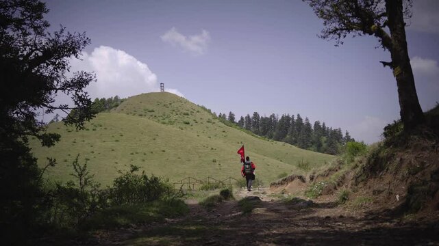 A Man waking in the greenery Meadow of Khaptad National Park with flag of Nepal, travelling in Farwest Nepal
