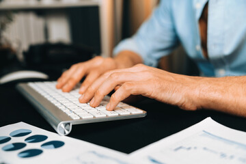 Cropped image of sales manager typing with keyboard with business paragraph dynamic data marketing analysis plan surrounded paper sheet and pc monitor report at home office at night. Pecuniary.