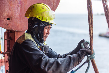 Seafarer securing a rope to a fitting, focused on safely preparing the pilot ladder. The tension in the hands reflects the importance of precision and safety in this critical task.