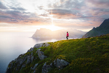 Breathtaking view of a young woman climber hiking on cliff over a stunning fjord landscape during a...