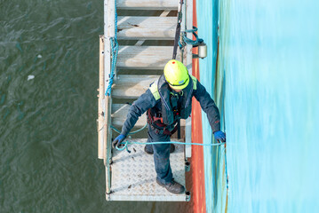A deckhand prepares the pilot ladder as the ship readies for port entry. Secured in a safety...