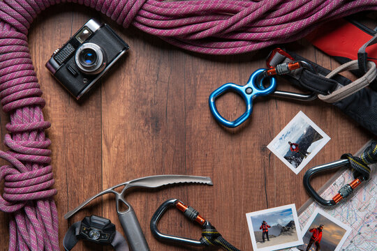 wooden table with climbing equipment, rope, carabiners, ice axe, map, headlamp, pocket knife, notebook and vintage camera with photos of man on summit