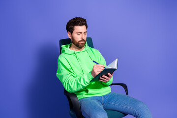 Photo portrait of attractive young man sit armchair write notebook dressed stylish green clothes isolated on violet color background