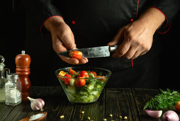 Knife in chef hand for cutting tomatoes. Cooking vegetable mix on kitchen table by cook hands.