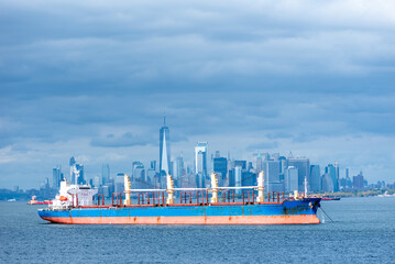 A cargo ship rests anchored in the bay, dominating the foreground. In the distance, the steel-blue...
