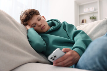 Loneliness concept. Sad teenage boy using smartphone on sofa at home © New Africa