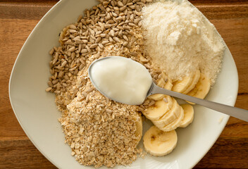 Close up of a deep plate with muesli ingredients, as oatmeal, sunflower seeds, banana slices,...