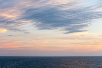 Pastel clouds drift across the sky, the colors blending softly into the horizon. The Atlantic Ocean below lies calm, reflecting the fading light as day gives way to night.