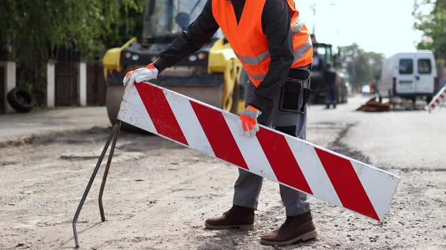Construction worker placing a road barrier during repair work on a residential street in broad daylight