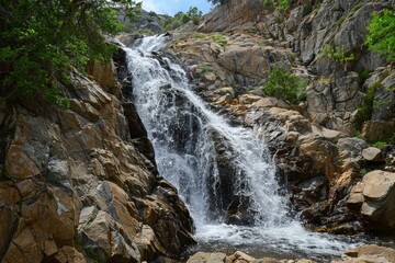 Fototapeta premium A serene waterfall cascades down rocky cliffs surrounded by lush greenery in a peaceful natural setting during daylight hours