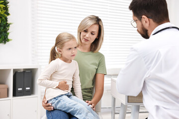 Obraz premium Doctor consulting little girl with stomach pain and her mother in hospital, back view