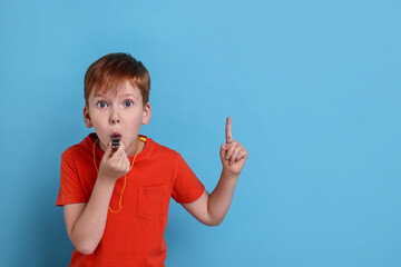 Little boy blowing whistle on light blue background, space for text