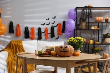 Halloween celebration. Pumpkin with creepy face, candles and flowers on wooden table in decorated room