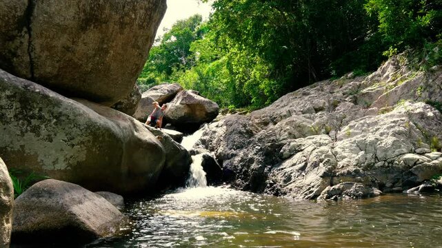 A tourist stands on a huge stone and washes himself from a mountain stream