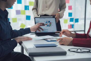 Fototapeta premium Business Strategy Meeting: A diverse team of professionals collaborates around a table, analyzing data on a tablet, showcasing teamwork, innovation, and collaboration in a modern office setting. 