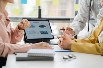 Strategic Business Meeting: A focused team collaborates around a tablet displaying key performance...