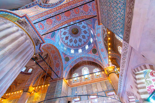 Interior view of the ornate walls and ceilings decorated with Iznik tiles and painted floral motifs of colorful blue, golden and red, inside the historic Blue Mosque in Istanbul, Turkey.