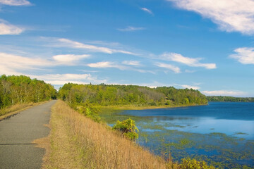 Early Autumn landscape of the Paul Bunyan Trail passing by a peaceful blue lake on a sunny day near Bemidji, Minnesota, USA.