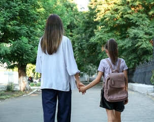 Mother and daughter holding hands outdoors, back view