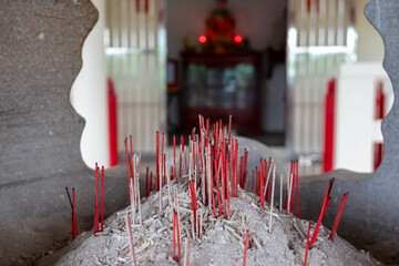 Close-up view of burner filled with burning incense sticks in a mound of gray ash in Chinese temple...